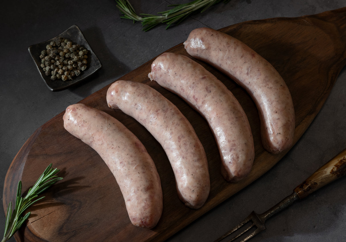 Un-cooked duck sausage links on a wooden board, with spices and herbs scattered around, and a glass of Sauternes wine in the background.